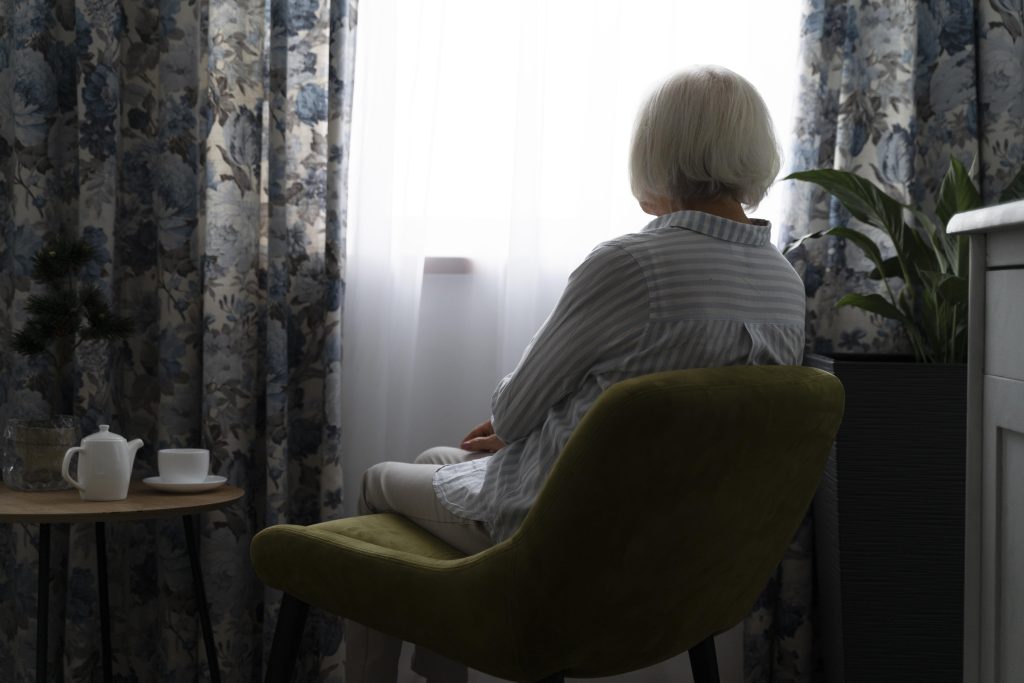 Elderly woman sitting alone by the window, reflecting in a quiet room